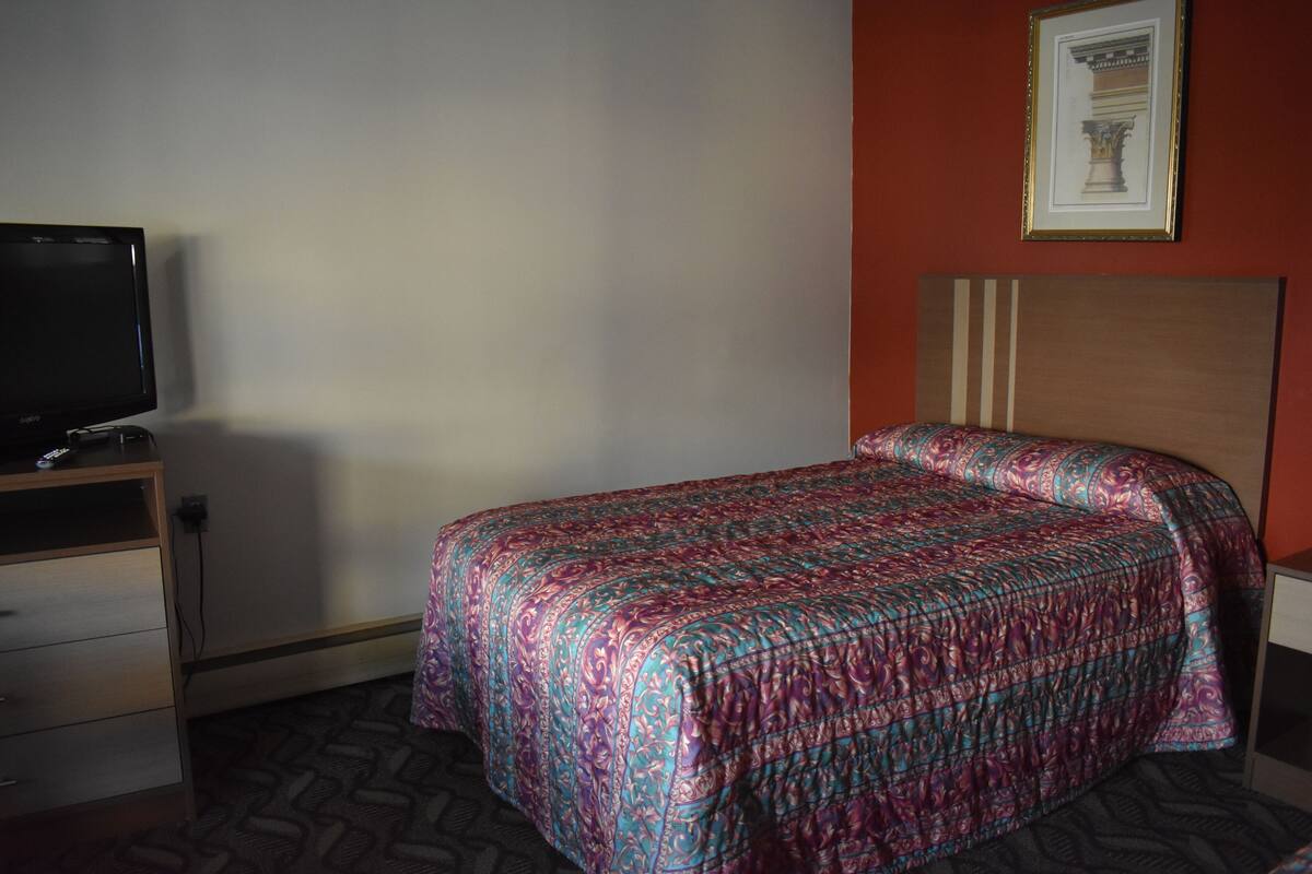 A hotel room with a bed, a television on a wooden dresser, and a framed picture on the wall.