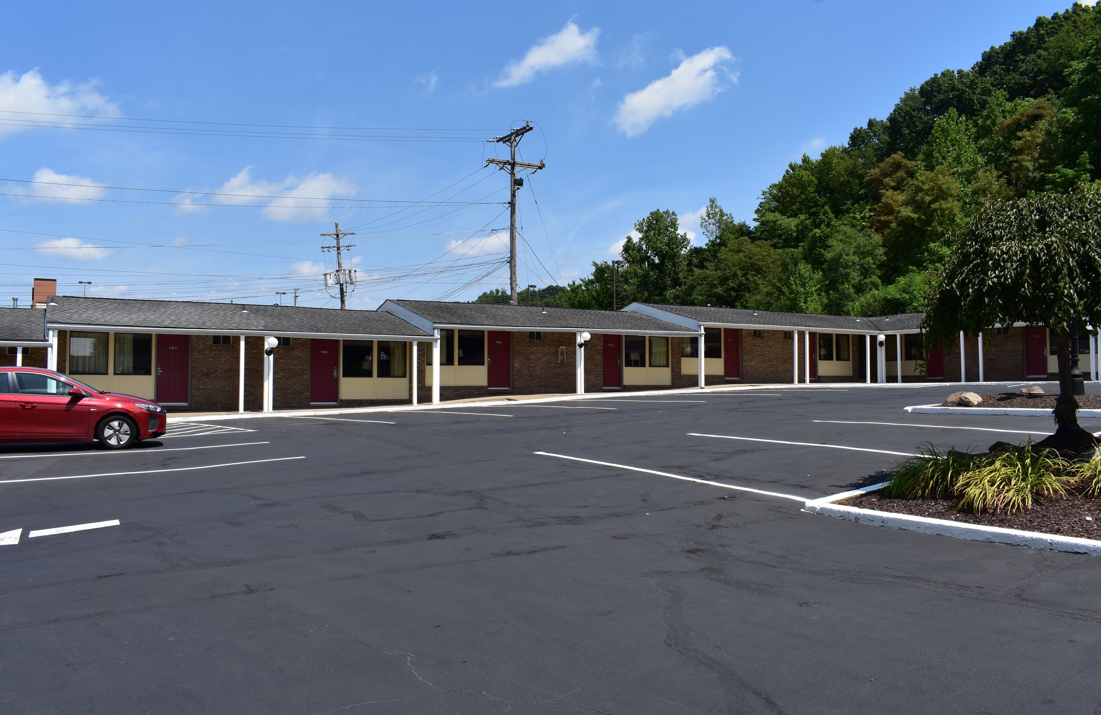 Un motel con varias habitaciones, un estacionamiento y un coche rojo estacionado al frente.