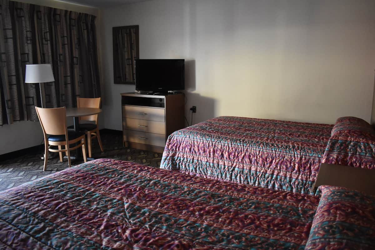 A hotel room with a bed, a desk with a chair, a television, and a lamp.