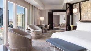 A modern hotel room with a large bed, two armchairs, a desk, and a view of the cityscape.
