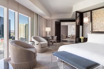 A hotel room with a large bed, a sofa, a TV, and a city view. at Waldorf Astoria Las Vegas