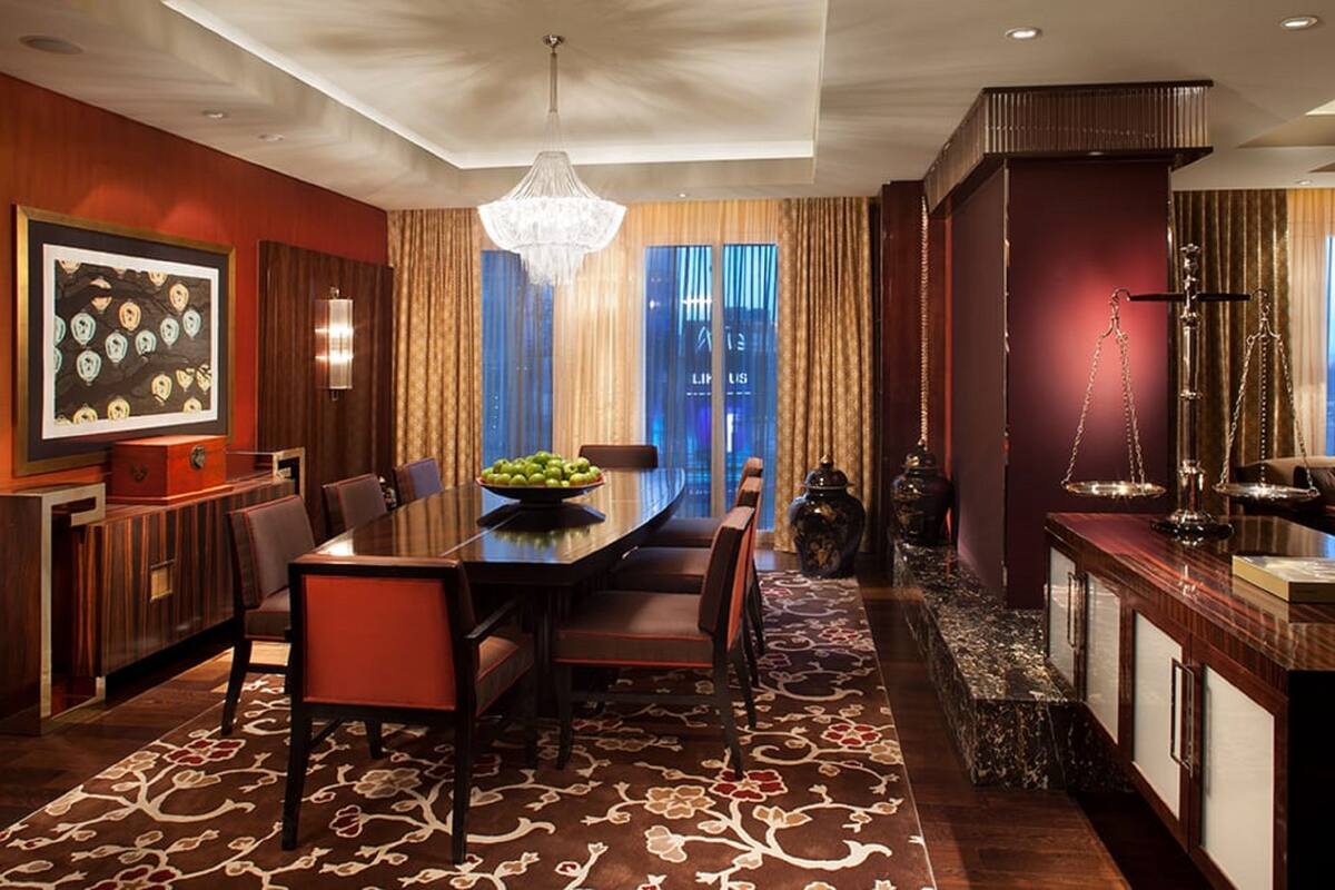 Un espace de restauration moderne dans un hôtel, avec une grande table, des chaises, un lustre et une vue sur le paysage urbain grâce à de grandes fenêtres.