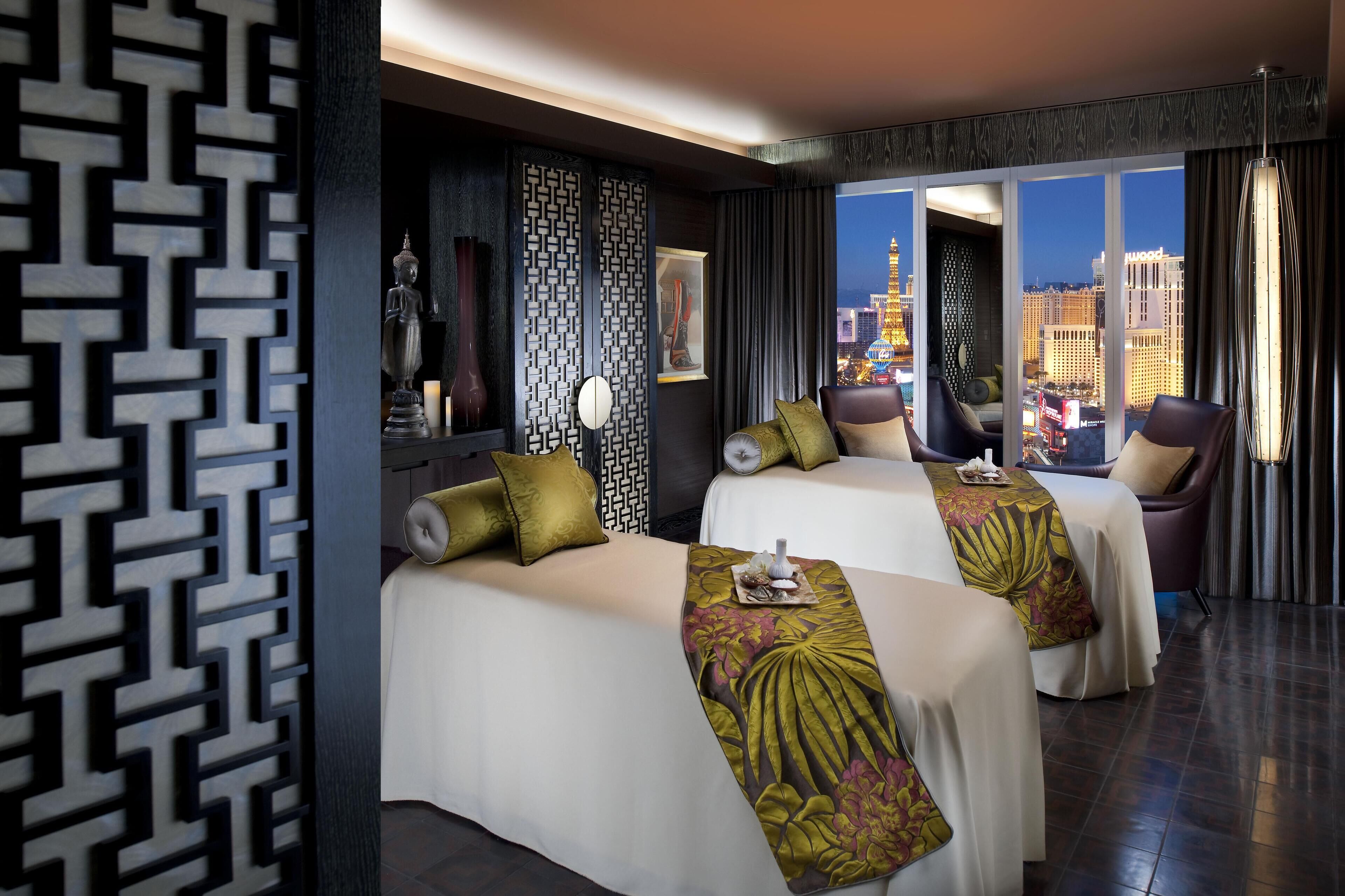 A hotel room with two beds, a view of the cityscape, and a decorative wall panel.