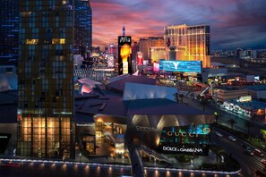 Une vue urbaine mettant en valeur des bâtiments remarquables, notamment l’hôtel Aria, un grand hôtel dont l’enseigne est illuminée, et le magasin Dolce & Gabbana.