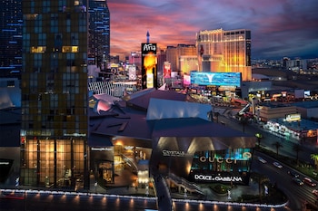 A modern hotel room with a large bed, two armchairs, a desk, and a view of the cityscape. at Waldorf Astoria Las Vegas