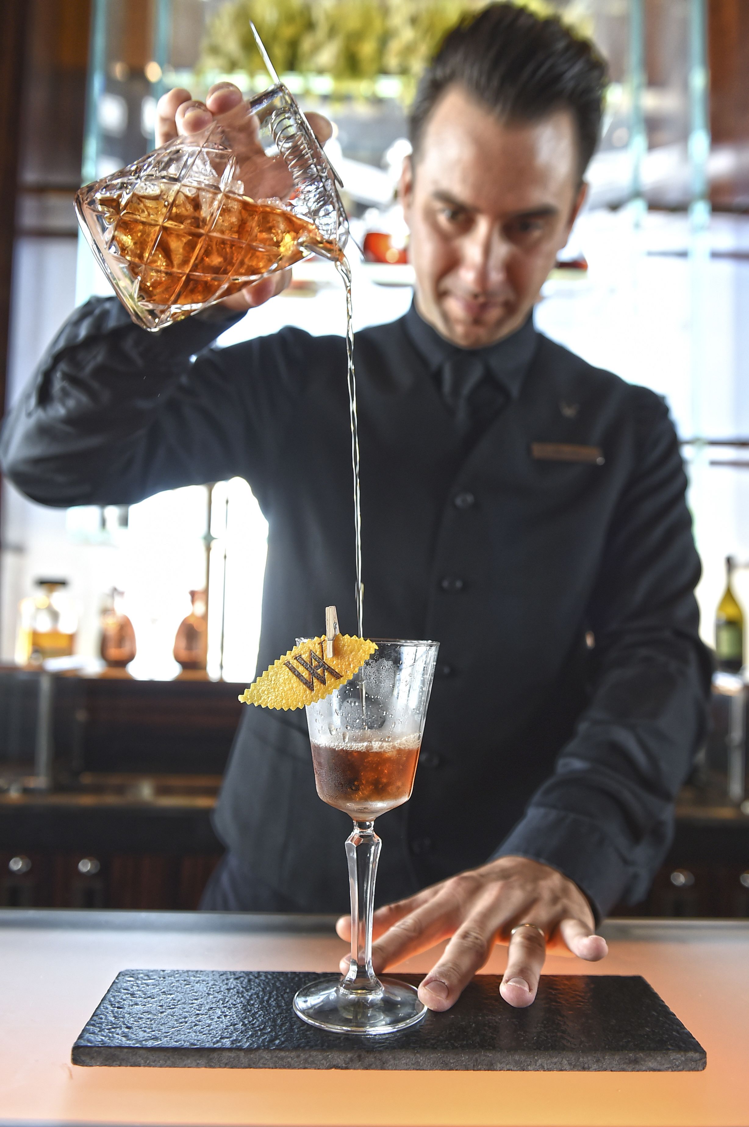Un barman verse une boisson dans un verre décoré d’une feuille.