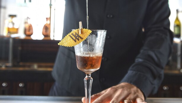 Een bartender schenkt een drankje in een glas met een decoratief blad.