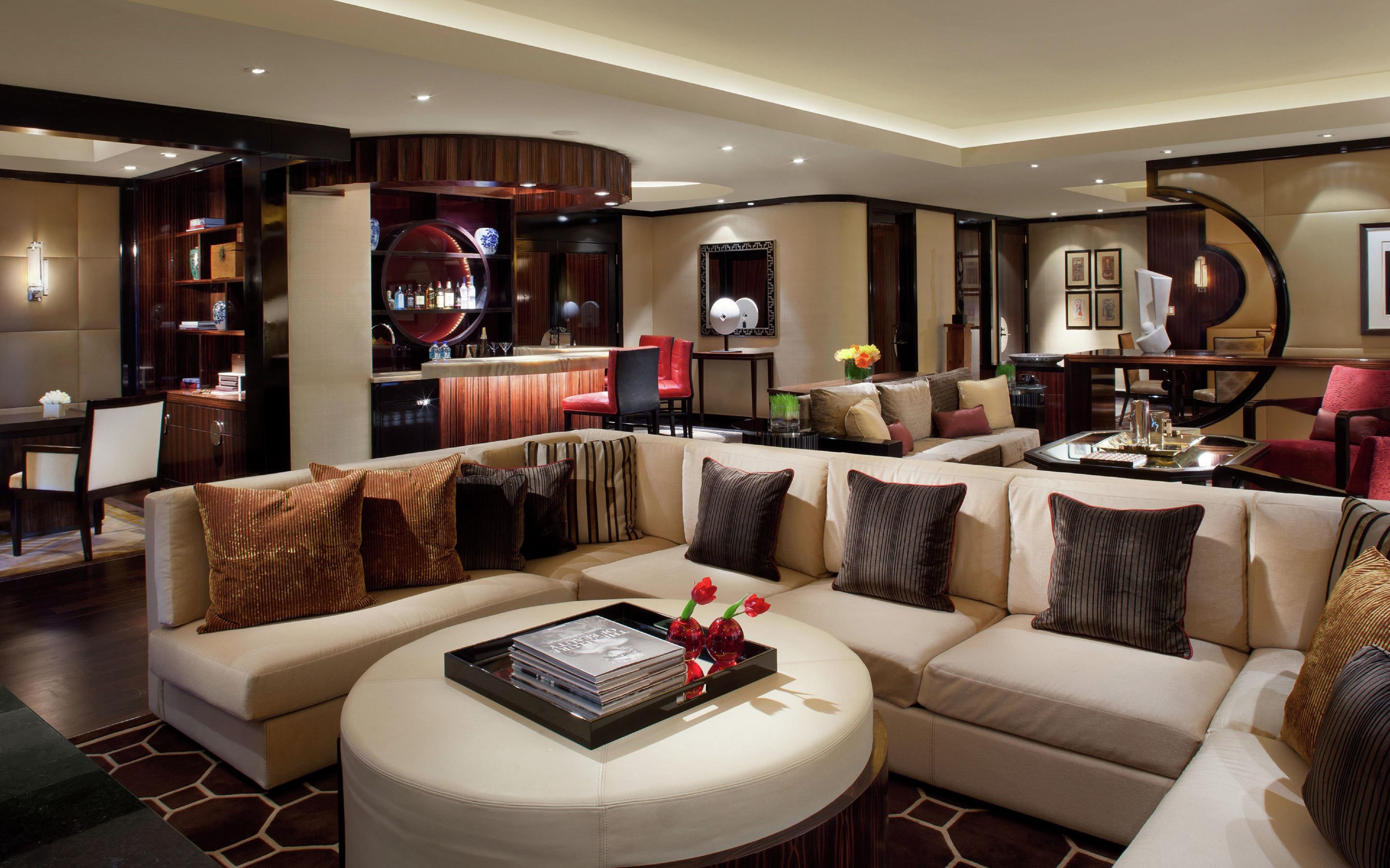 A modern living room with a sectional sofa, a round coffee table, and a bar area with red chairs.