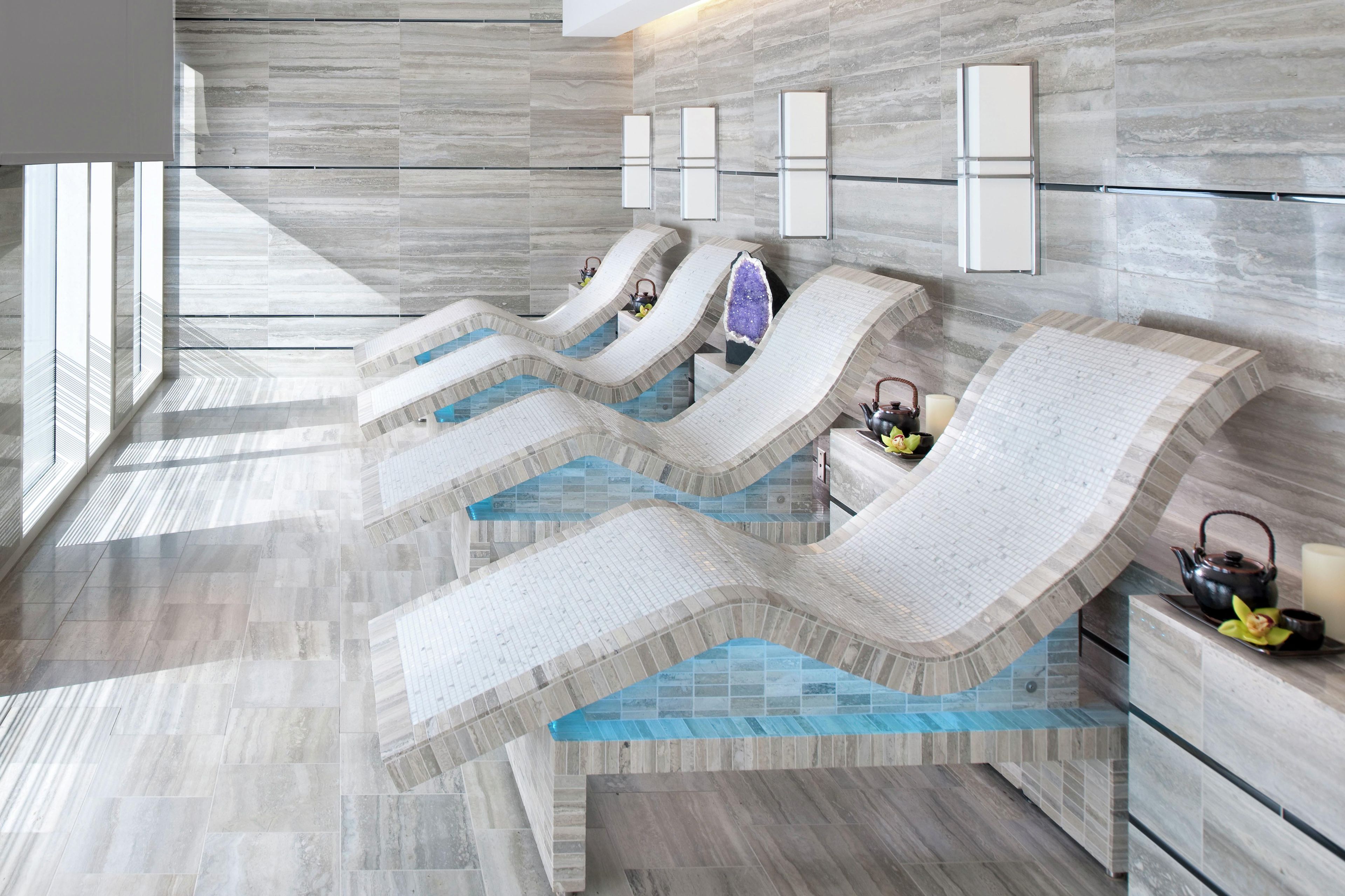 A modern spa area with multiple hot tubs, a marble floor, and wall-mounted lighting.