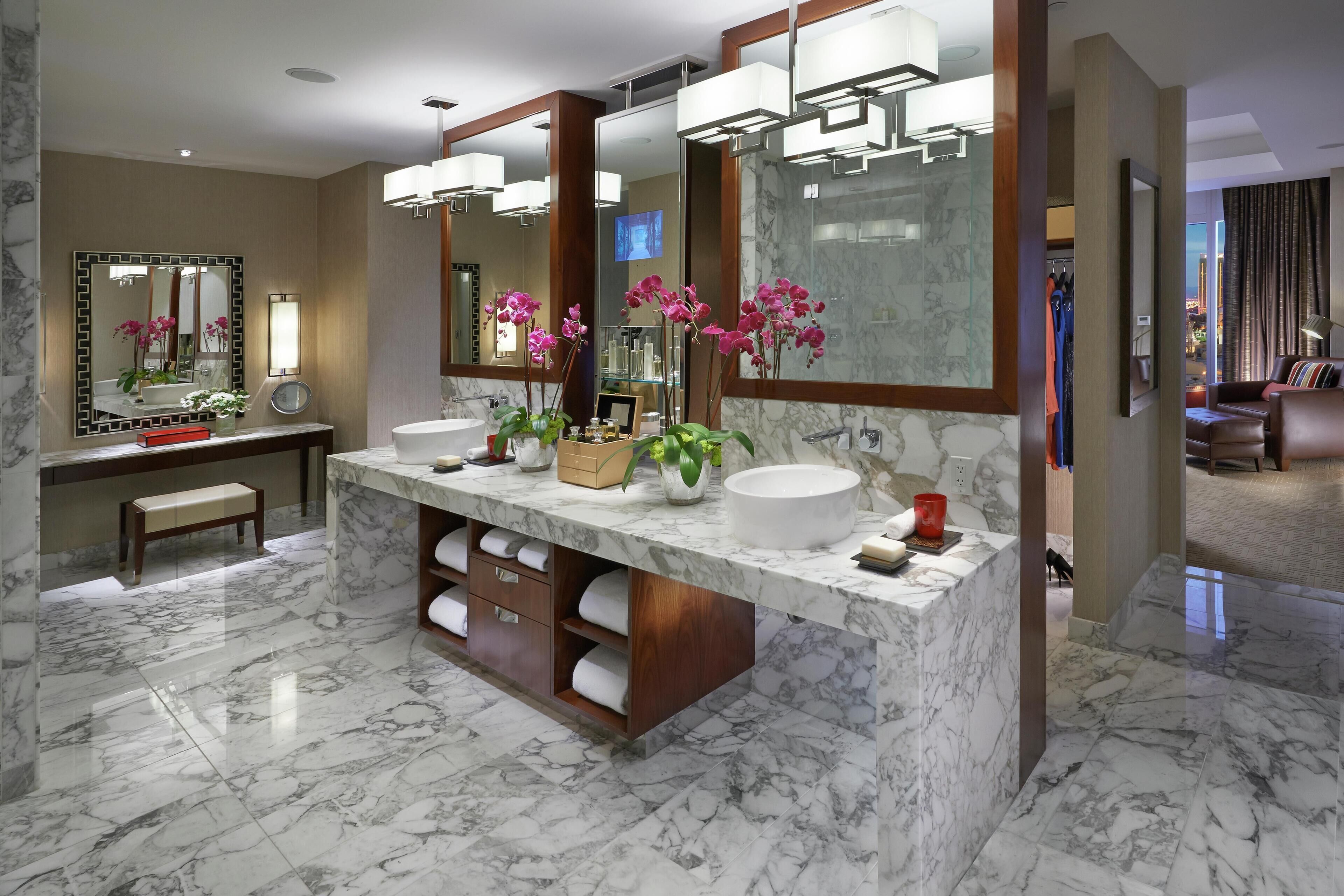 A modern bathroom with two sinks, marble flooring, and large mirrors.