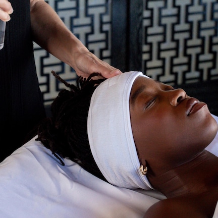 A person lying on a bed with a white pillow and headband, receiving a massage from another person.