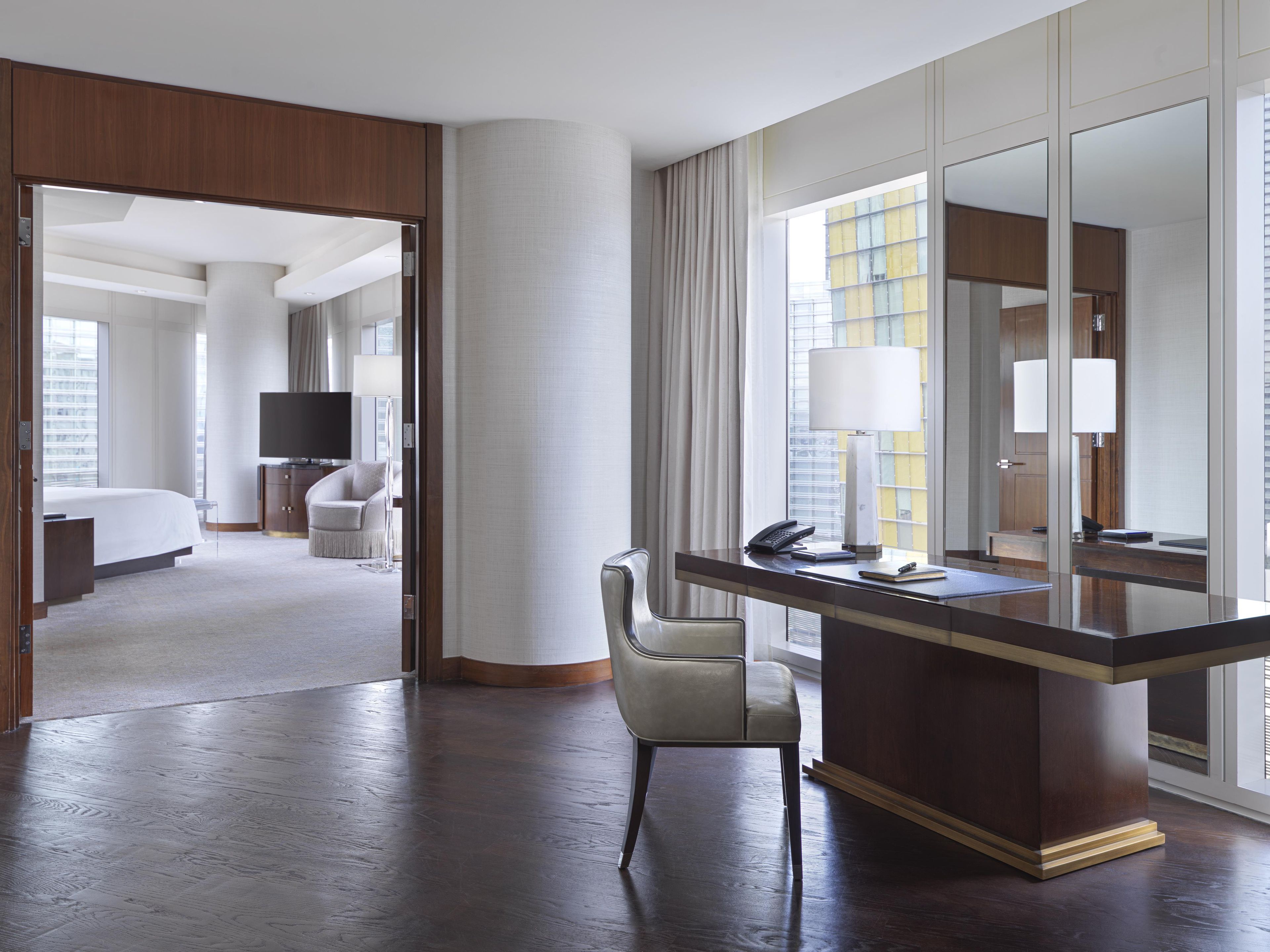 A hotel room with a bed, a desk with a chair, a television, and a large mirror.