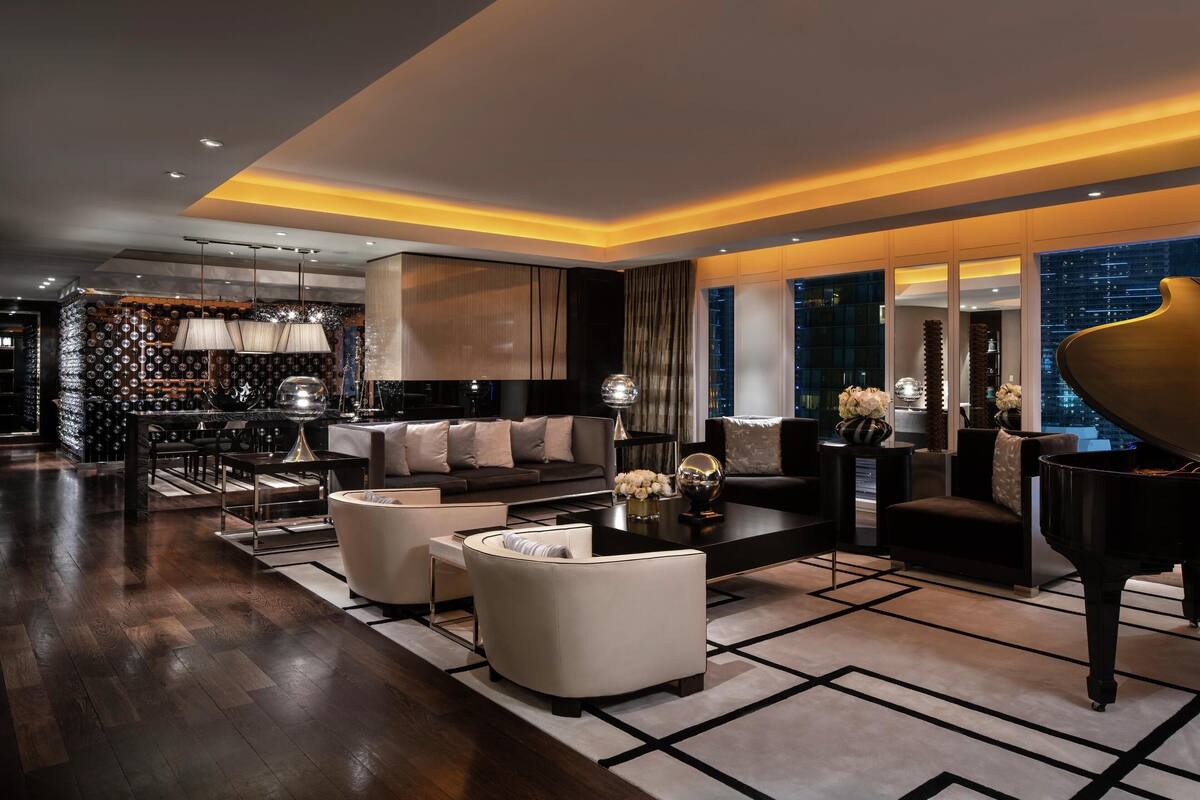 Un salon moderne avec un grand piano, un ensemble de canapés et un coin repas agrémenté d’un mur à motifs et d’un éclairage suspendu.