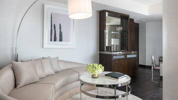 Un salon moderne avec un canapé beige, une table basse ronde sur laquelle reposent un livre et des fleurs, un grand lampadaire et un meuble avec des portes en verre.