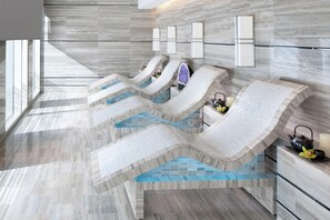 A modern spa area with multiple hot tubs, a marble floor, and wall-mounted lighting.