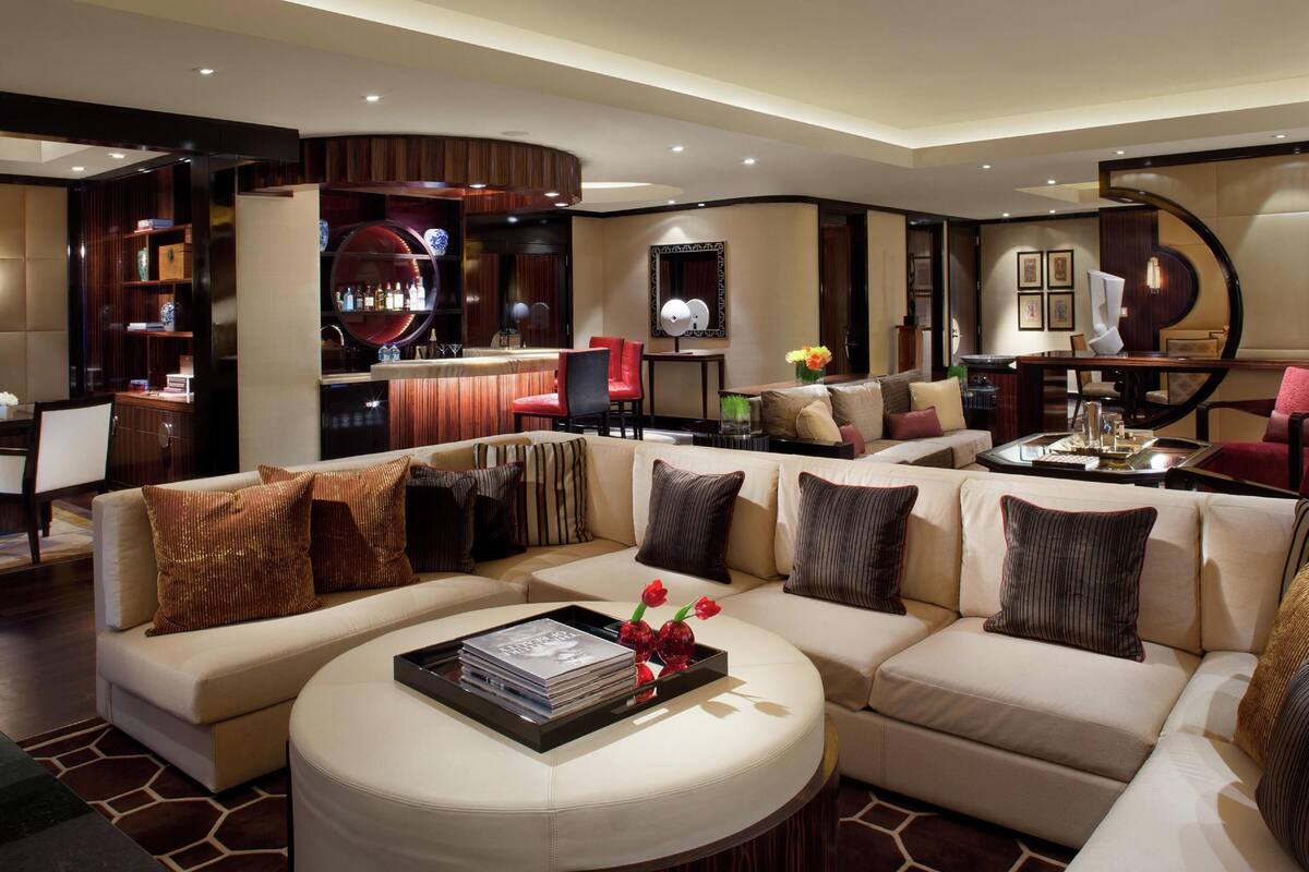 Un salon moderne avec un canapé d’angle, une table basse ronde et un coin bar avec des chaises rouges.