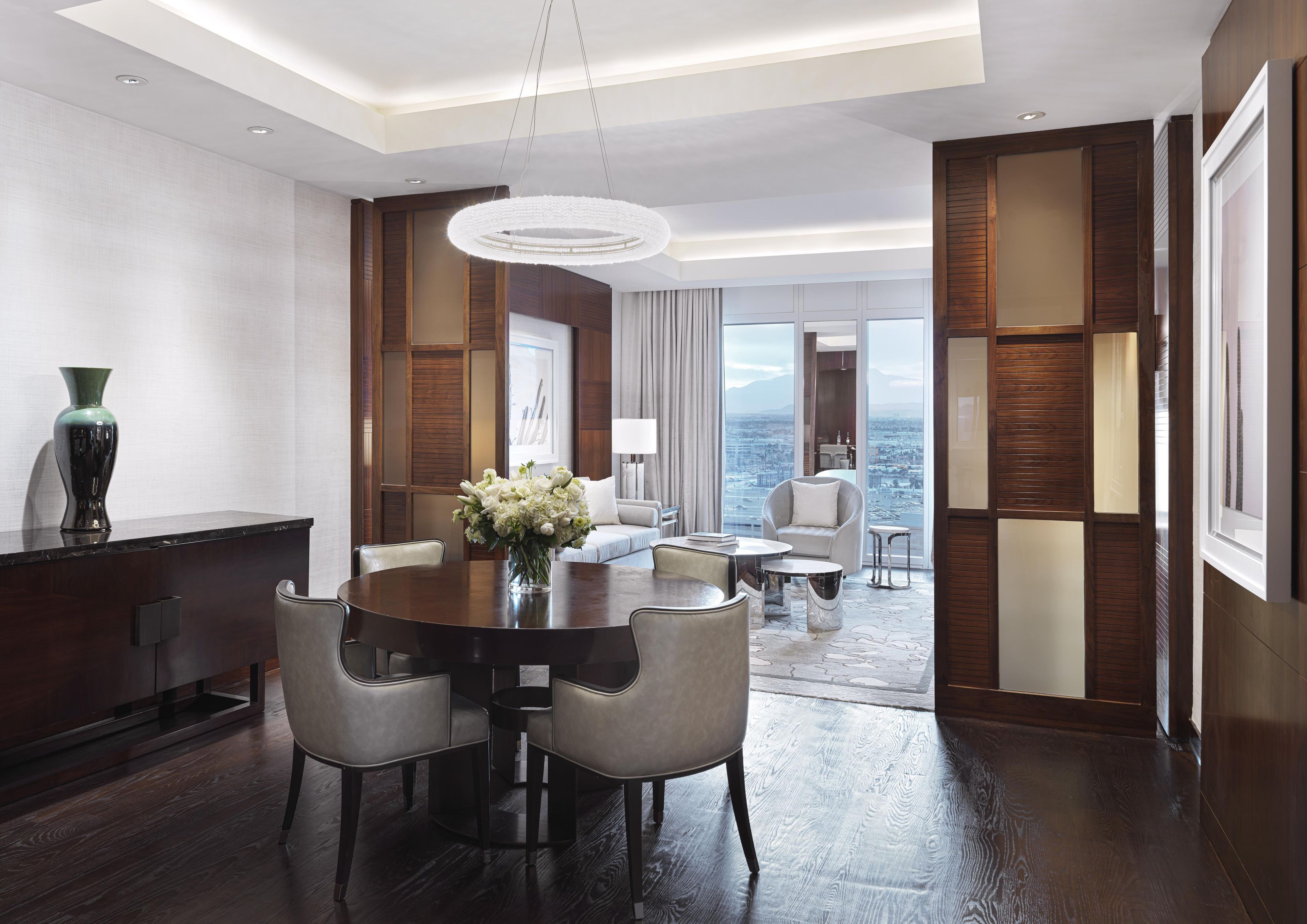 A modern hotel room with a dining area, a sofa, a chair, and a view of the city.