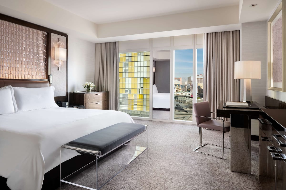 Une chambre d’hôtel équipée d’un lit, d’un bureau, d’une chaise et offrant une vue sur la ville grâce à de grandes fen êtres.