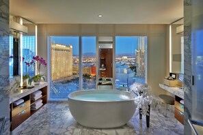 Un baño moderno con una bañera grande, suelo de mármol y vistas a la ciudad a través de ventanales de gran altura.