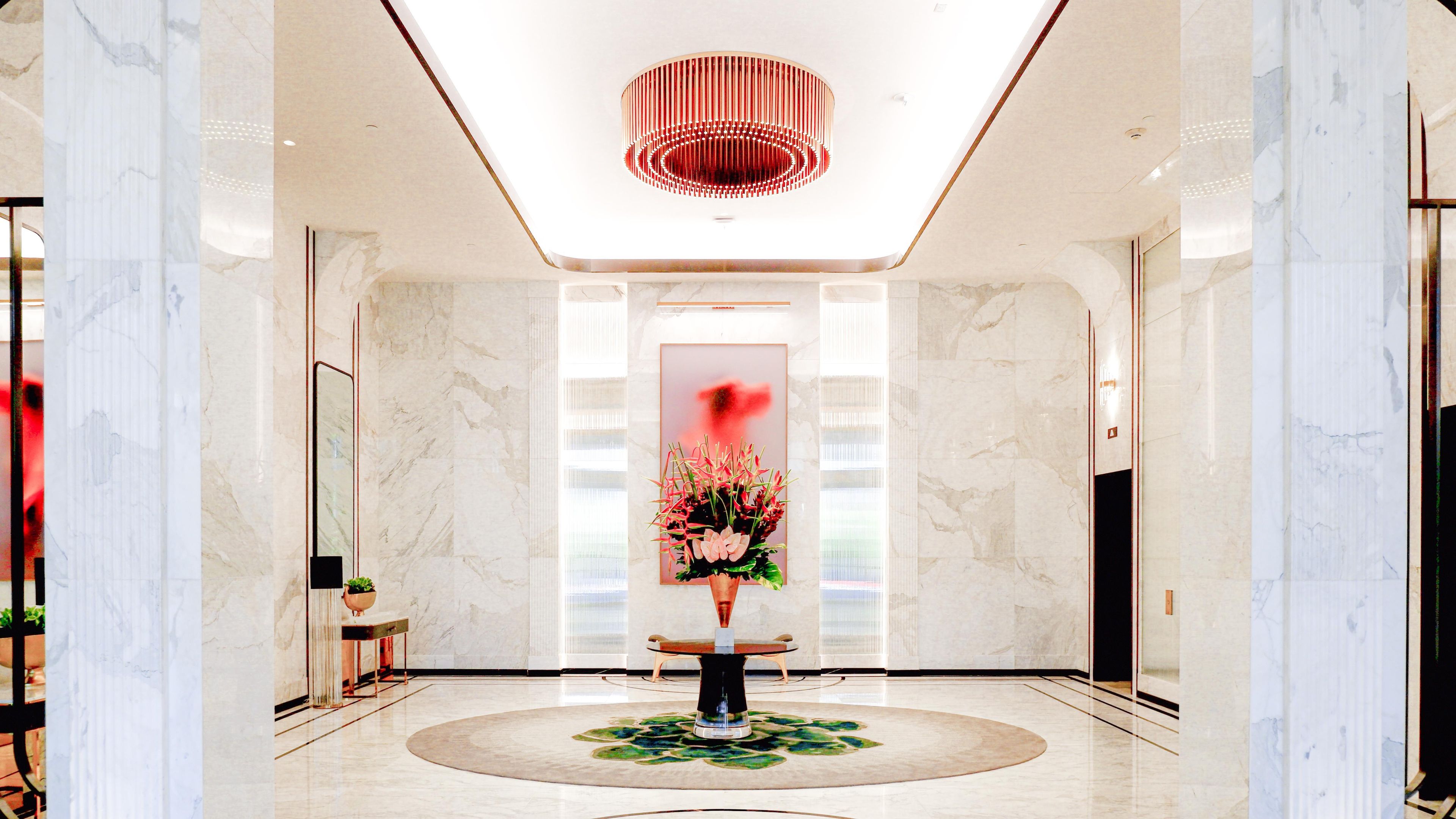 A modern lobby with a marble floor, a central floral arrangement, and a unique ceiling light fixture.