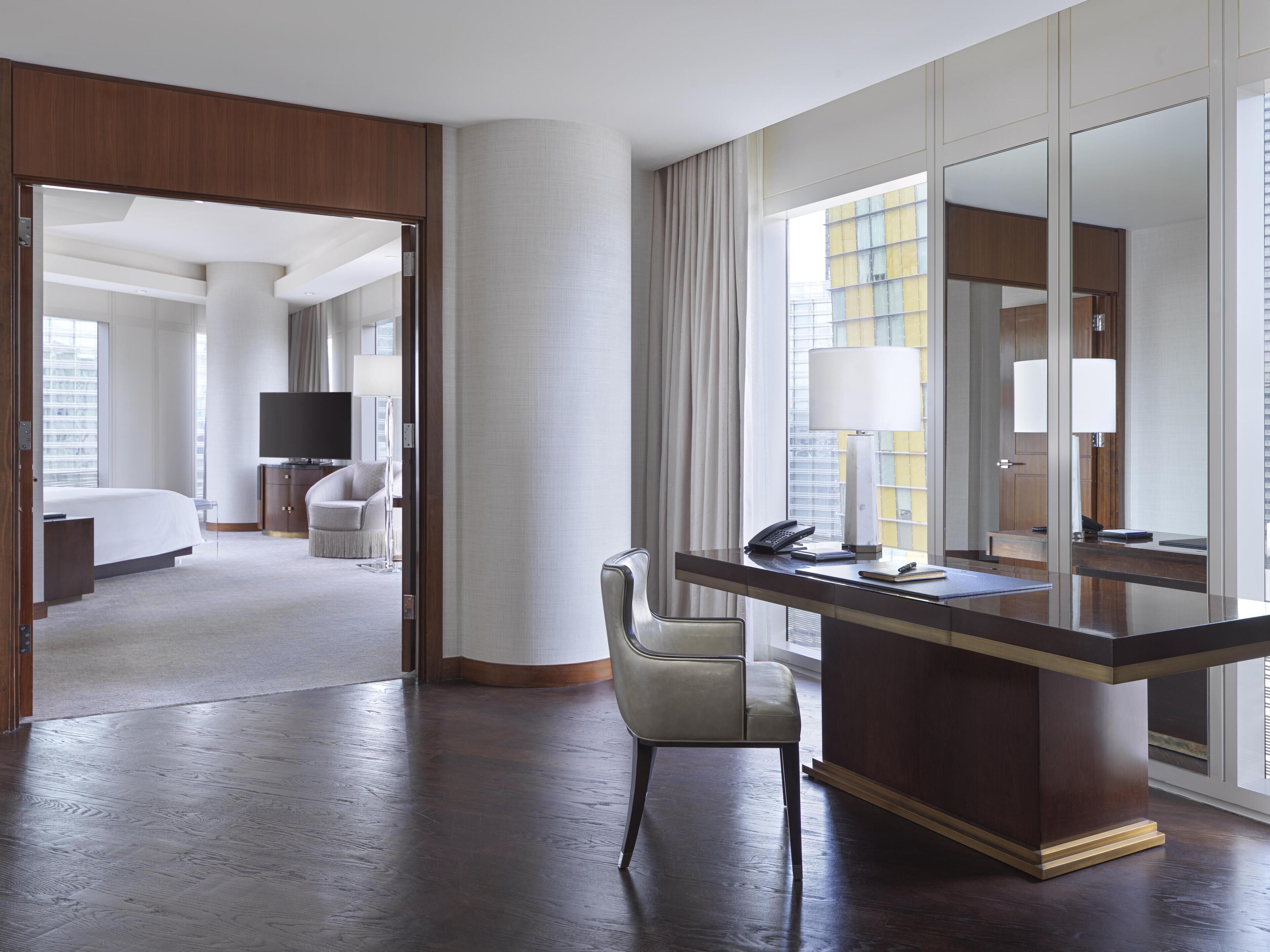 A hotel room with a large bed, a desk with a chair, a TV, and a window with curtains.