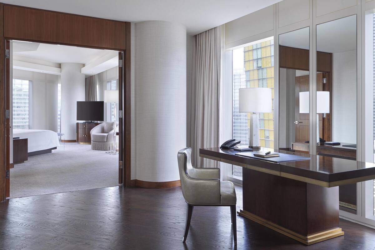 Une chambre d’hôtel avec un grand lit, un bureau avec une chaise, une télévision et une fenêtre avec des rideaux.