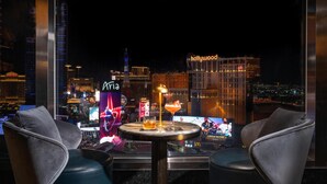 A bar area with two leather chairs and a round table, featuring a cityscape view with illuminated buildings in the background. - Waldorf Astoria Las Vegas (Las Vegas)
