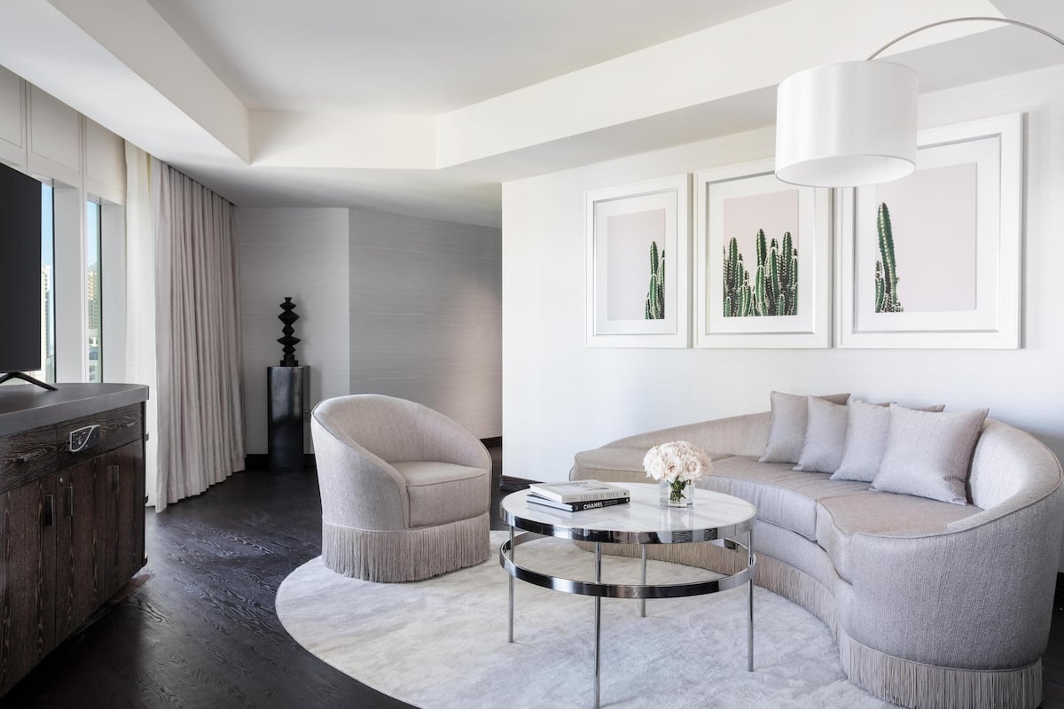 Un salon moderne avec un canapé, un fauteuil et une table basse ronde. Des tableaux encadrés ornent le mur, et un lustre est suspendu au plafond.