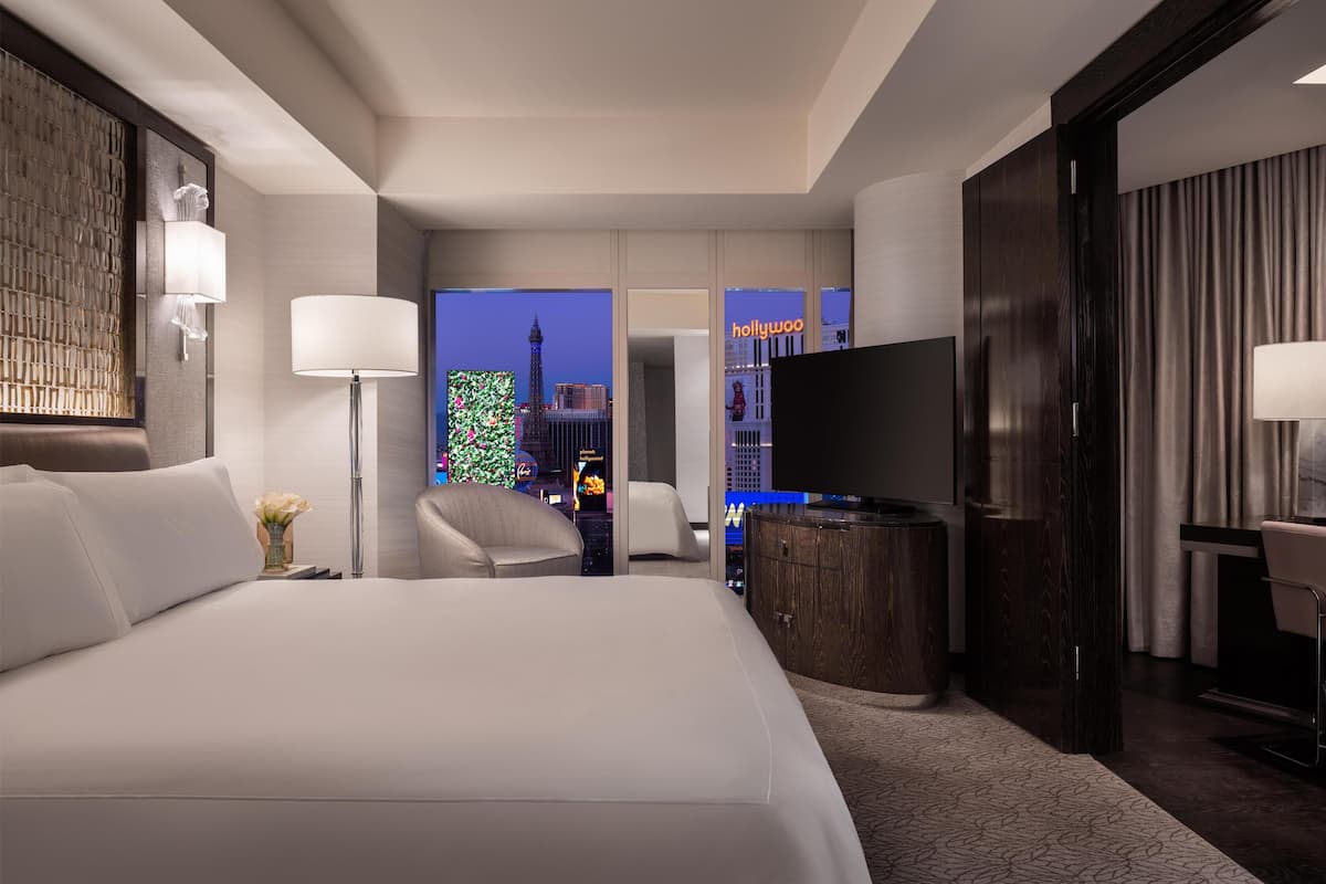 Une chambre d’hôtel moderne dotée d’un grand lit, d’une télévision à écran plat, d’un bureau et offrant une vue sur le paysage urbain.