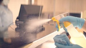 A person wearing blue gloves using a spray bottle to clean a surface. - Roadside Motel (Sheridan)