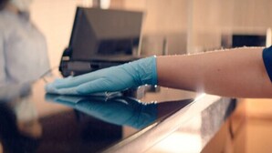 A person wearing blue gloves cleaning a reflective surface, likely a table or counter. - Roadside Motel (Sheridan)