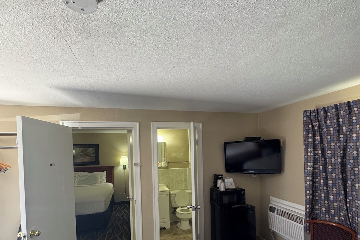 Habitación de hotel con cama, televisión, aire acondicionado y baño a la vista a través de una puerta abierta.