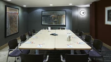 Une salle de conférence avec une longue table, des chaises et un grand tableau abstrait accroché au mur.