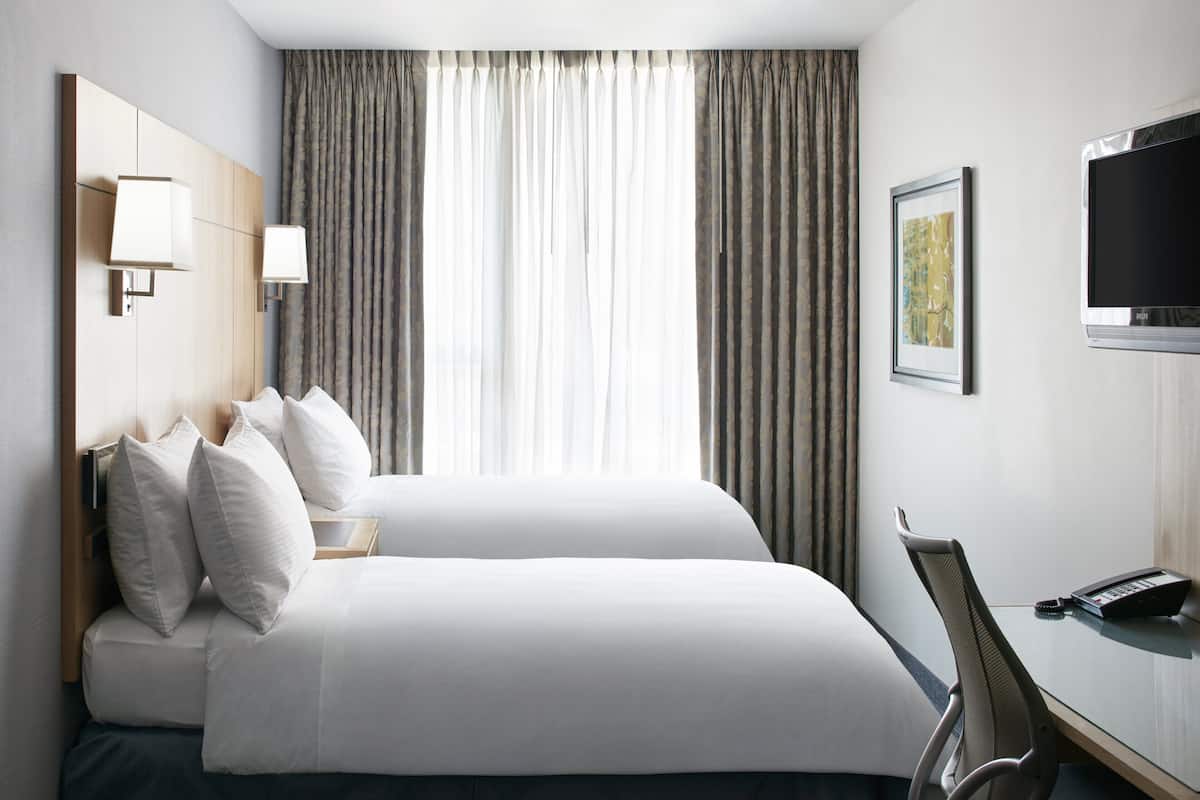 A hotel room with a large bed, a desk with a chair, a TV, and a framed picture on the wall.