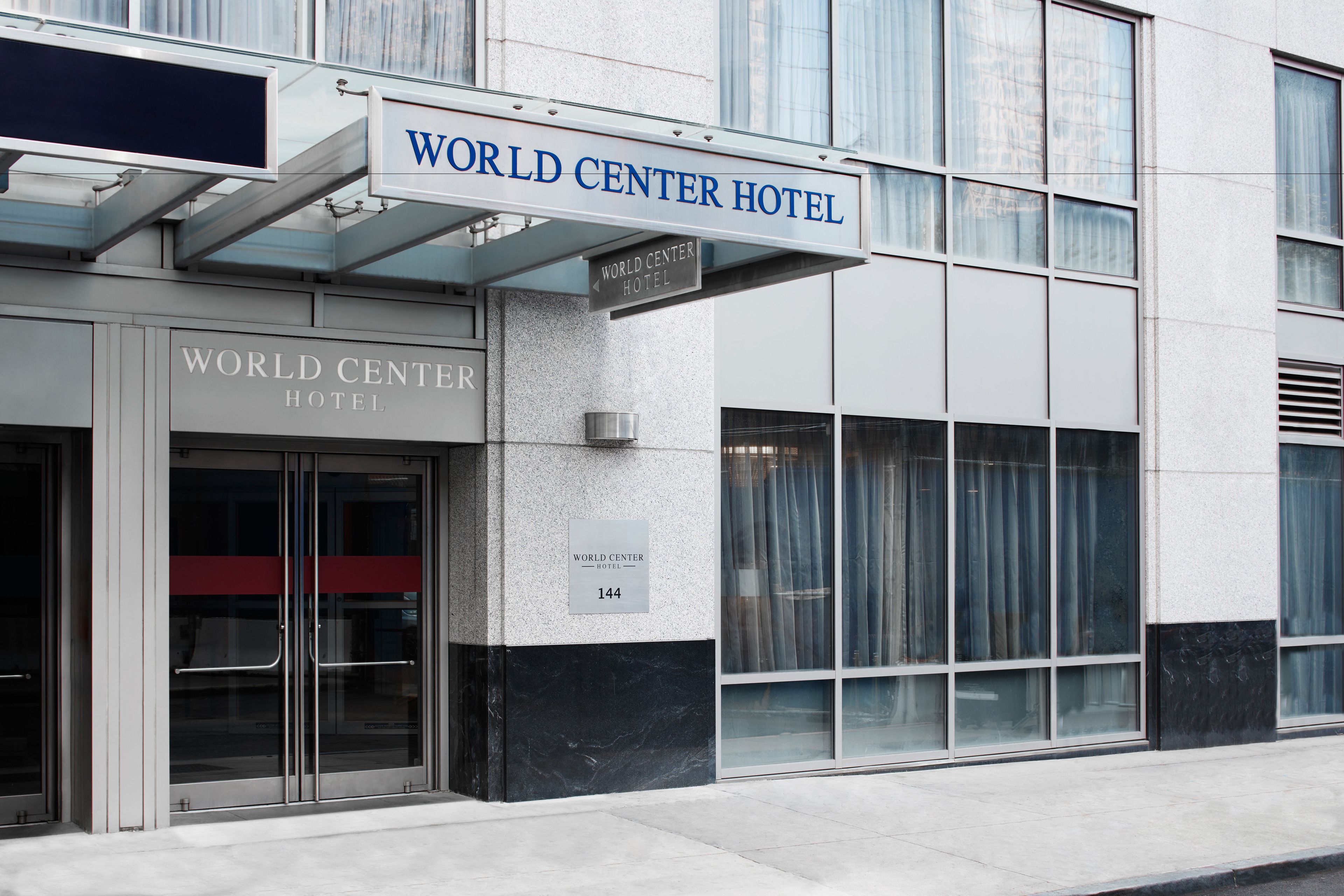 L’extérieur du World Center Hotel se distingue par une enseigne bien visible, une entrée en verre et une adresse clairement indiquée par des chiffres.