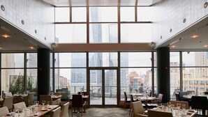 A spacious restaurant with large windows offering city views, multiple tables and chairs, and a modern interior design. - World Center Hotel (New York)