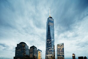 Une vue urbaine avec un gratte-ciel imposant, surmonté d’une flèche, entouré d’autres immeubles de grande hauteur.
