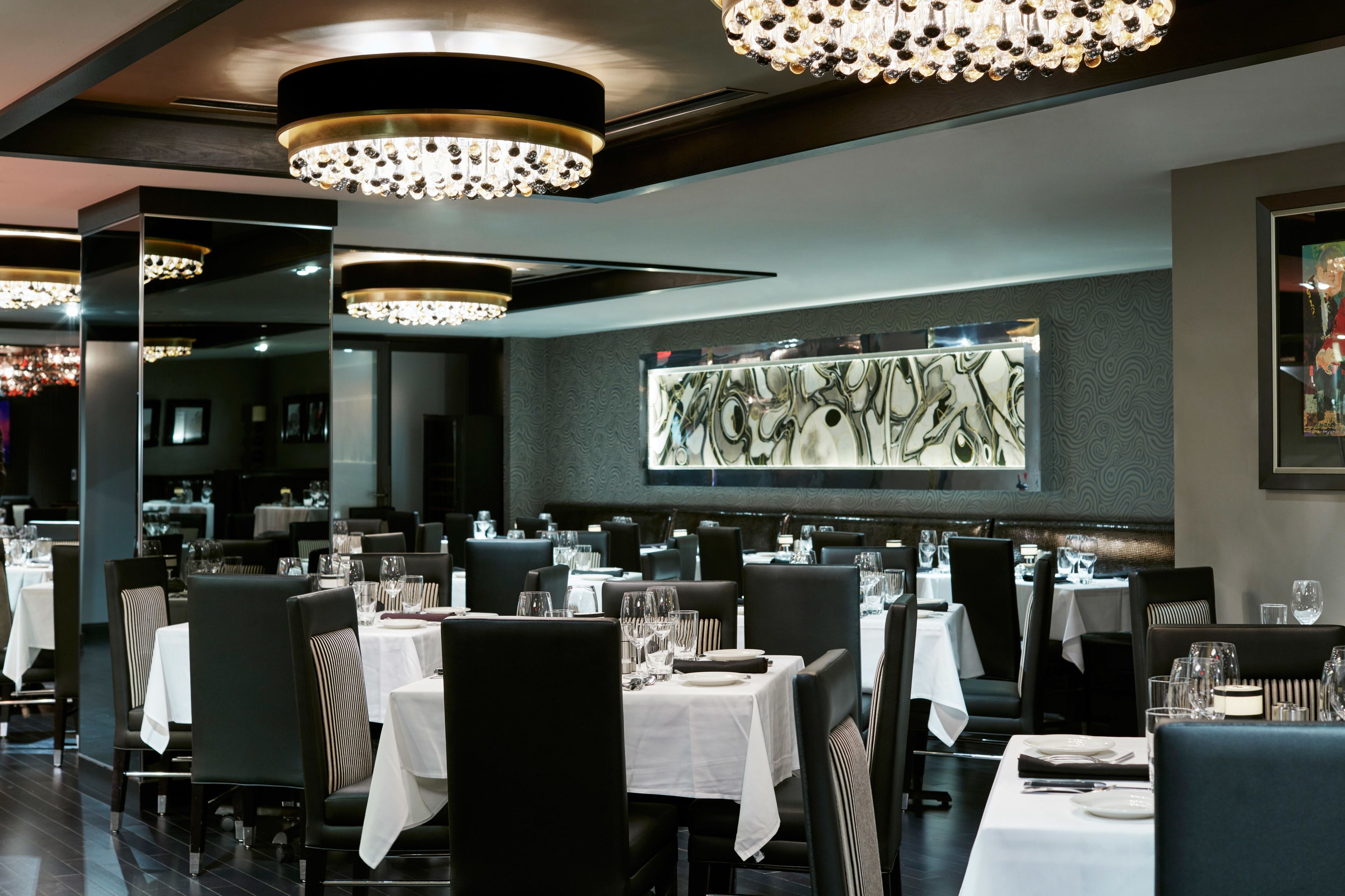 Un interno di ristorante con diversi tavoli, sedie nere e lampadari.