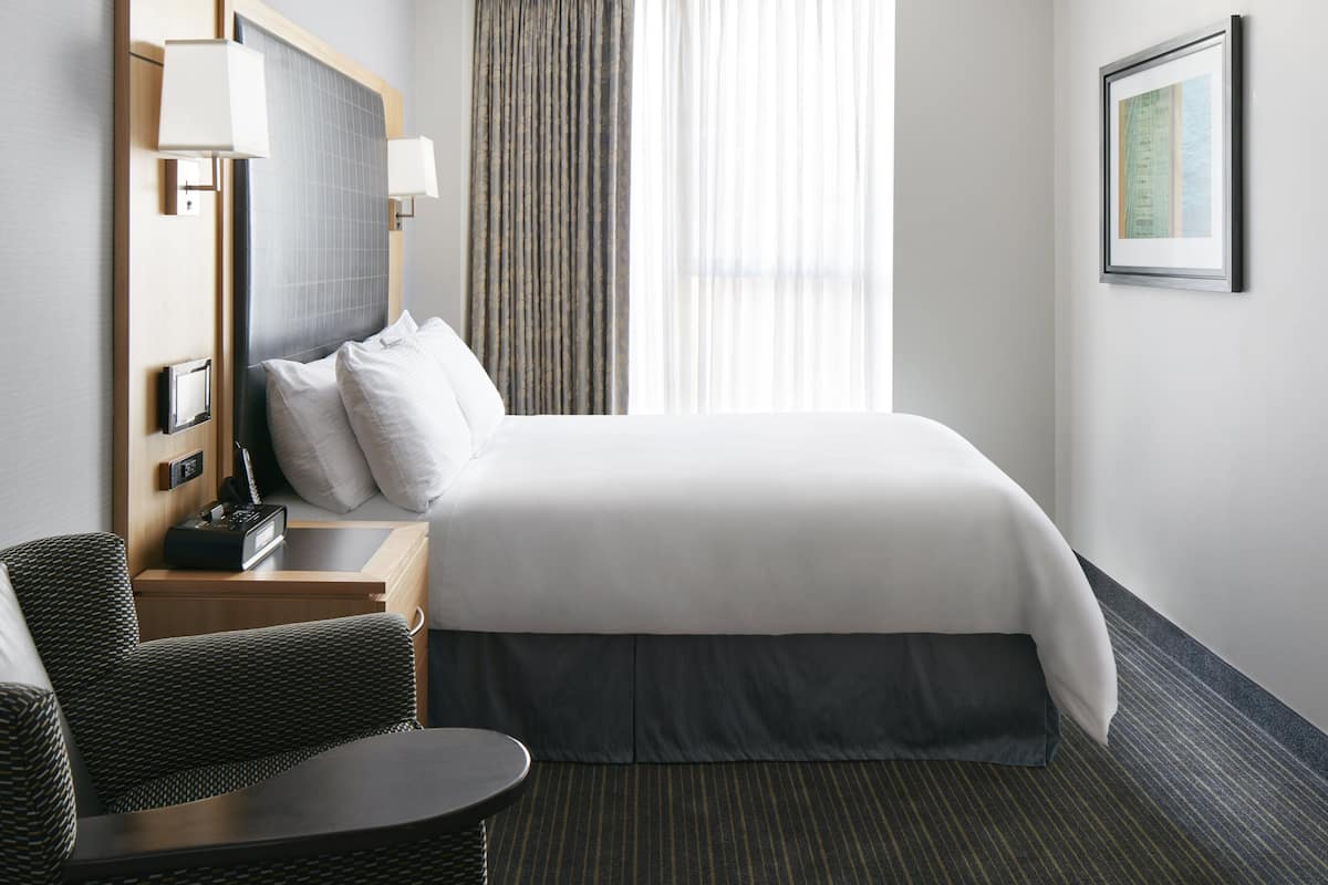 A hotel room with a large bed, a chair, a small table, a lamp, and a framed picture on the wall.