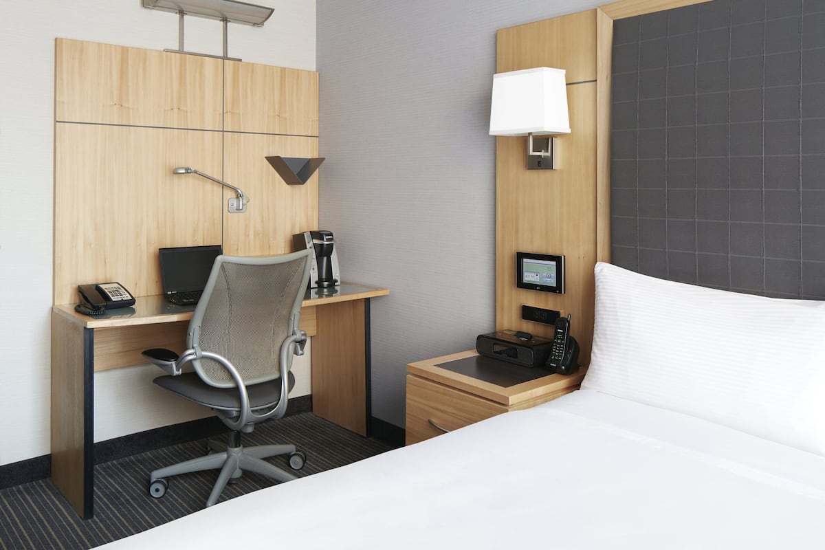 A hotel room with a bed, a desk with a computer, a chair, a telephone, a lamp, and a small table with a lamp.