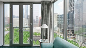 A hotel room with a large window, a sofa, a lamp, and a view of the cityscape. - World Center Hotel (New York)