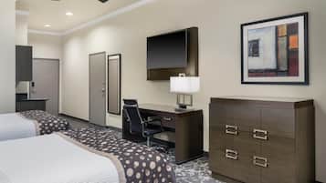 A hotel room with two beds, a desk, a chair, a TV, a cabinet, and a painting on the wall.
