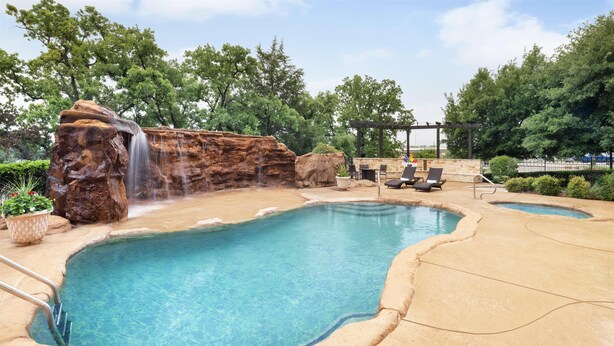 A pool area with a waterfall feature, lounge chairs, and a pergola. - Best Western Premier Crown Chase Inn & Suites (Denton)
