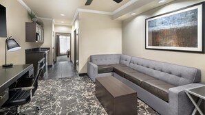 A modern hotel room with a sectional sofa, a desk with a chair, a standing lamp, and a ceiling fan. - Best Western Premier Crown Chase Inn & Suites (Denton)