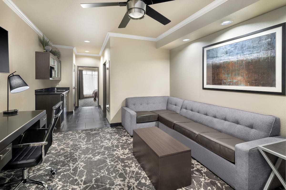 A modern hotel room with a sectional sofa, a desk with a chair, a standing lamp, and a ceiling fan.