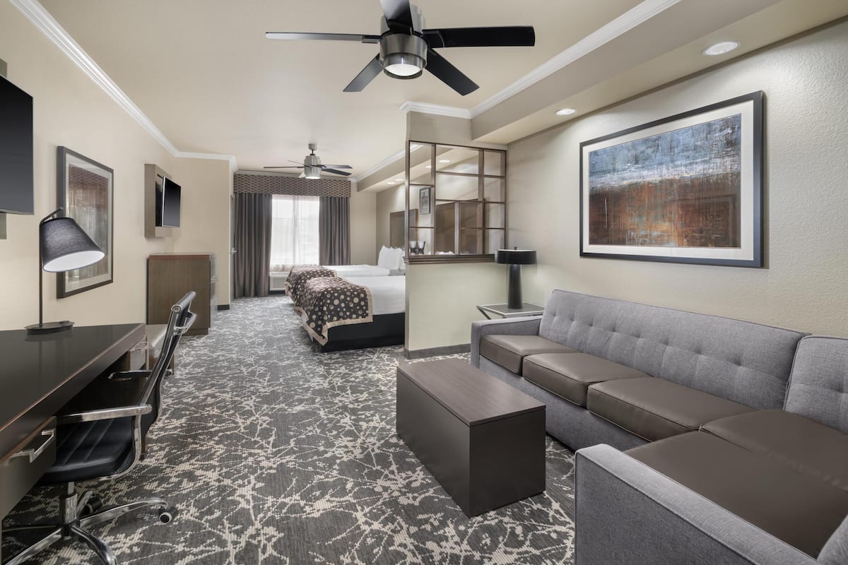 A hotel room with a bed, a sofa, a desk, and a ceiling fan.