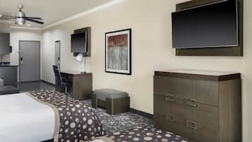 Habitación de hotel con cama, escritorio, silla, armario, televisor de pantalla plana, ventilador de techo y un cuadro en la pared.
