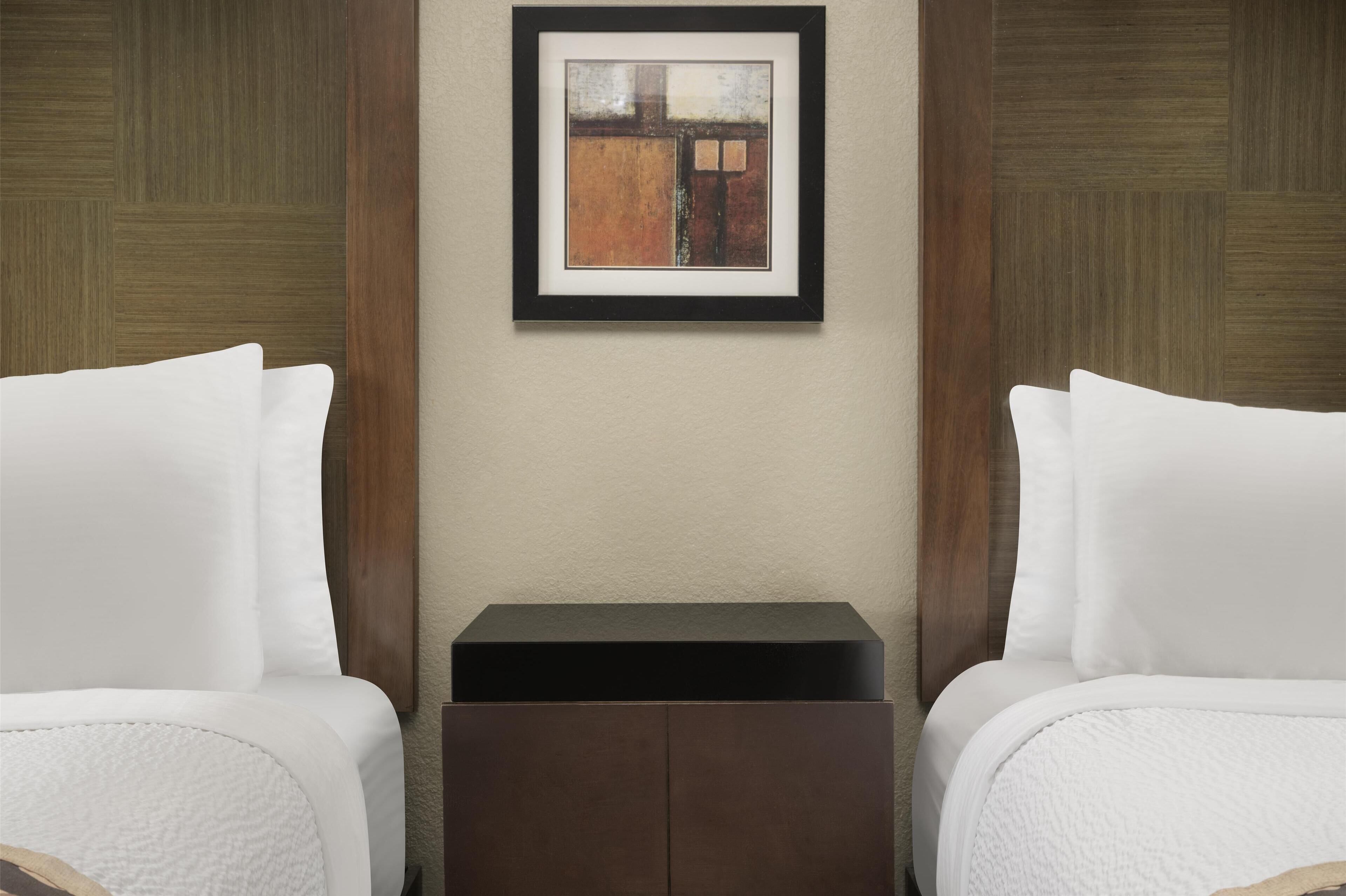 A hotel room with two beds, a small bedside table, and a framed artwork on the wall.