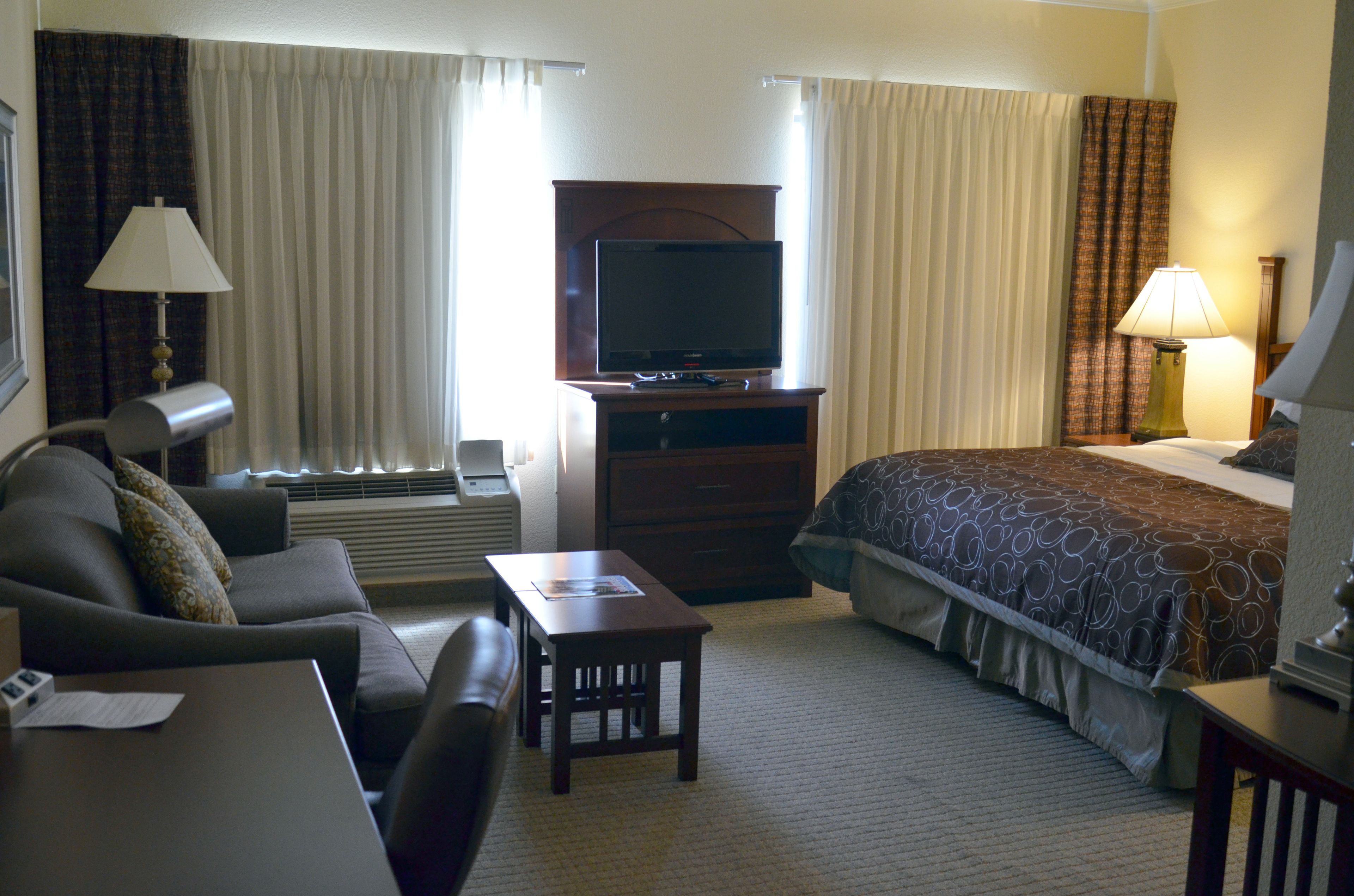A hotel room with a bed, a desk, a television, a sofa, and a lamp.