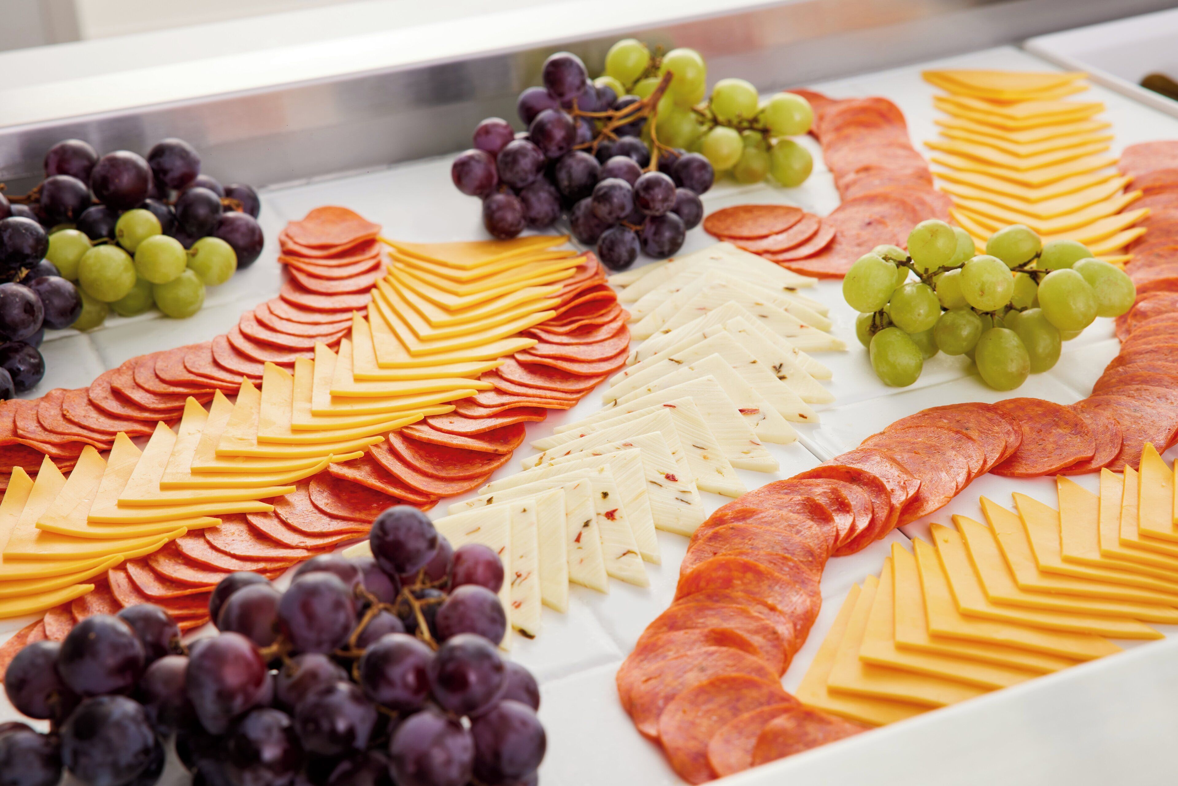 Une planche de charcuterie avec des viandes et des fromages en tranches, ainsi que des raisins.